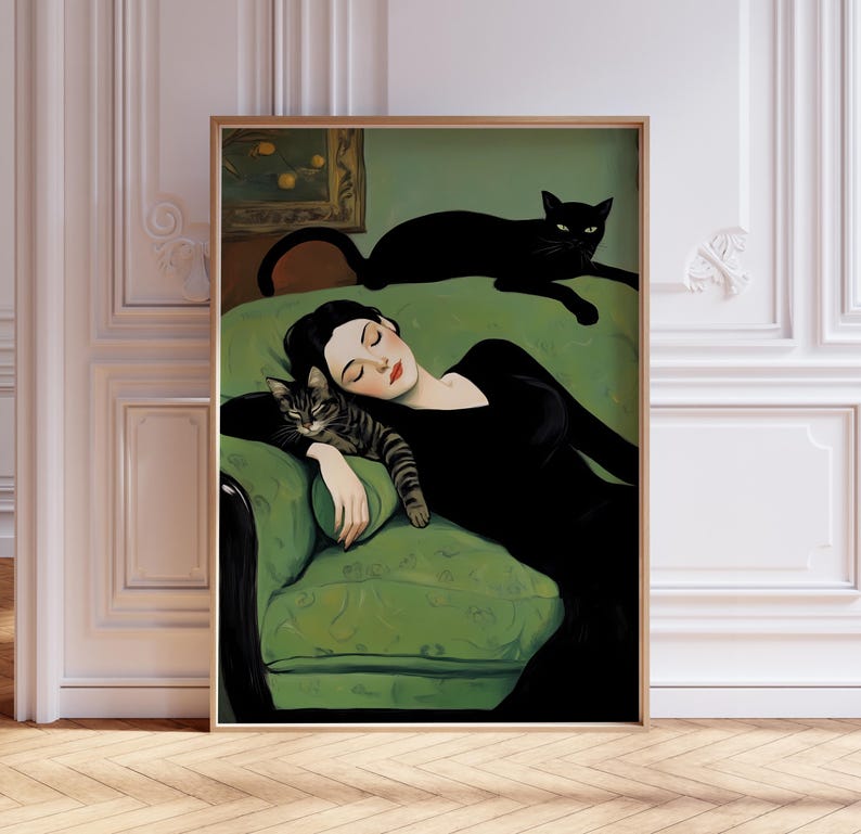 May include: A framed art print depicts a woman in a black dress reclining on a green sofa with two cats. One cat is striped and resting on the woman's arm, while the other is black and lounging on the sofa's back. The artwork has a vintage aesthetic.