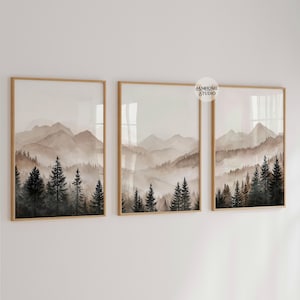 May include: A set of three framed wall art prints featuring a continuous landscape of misty mountains and dark evergreen pine trees in shades of brown, beige, and black. Each rectangular frame is made of light wood and displays a watercolor-style scene.