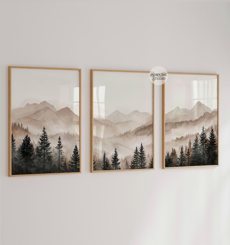 May include: A set of three framed wall art prints featuring a continuous landscape of misty mountains and dark evergreen pine trees in shades of brown, beige, and black. Each rectangular frame is made of light wood and displays a watercolor-style scene.