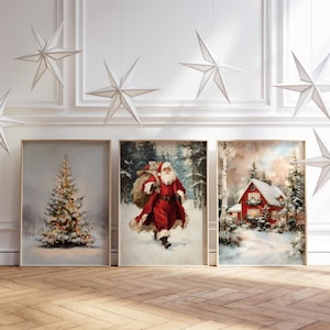 Op de afbeelding: Drie ingelijste kunstprints met kerstthema. Eén toont een versierde kerstboom, een andere toont de kerstman in een besneeuwd bos en de derde een rood huis in een winterlandschap. Witte sterdecoraties hangen erboven.