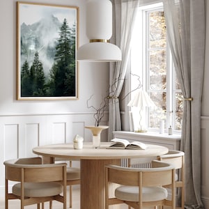May include: A round wooden dining table with a fluted base and four chairs. The chairs have light brown wood frames and beige upholstery. A framed print of a misty mountain scene hangs on the wall behind the table.