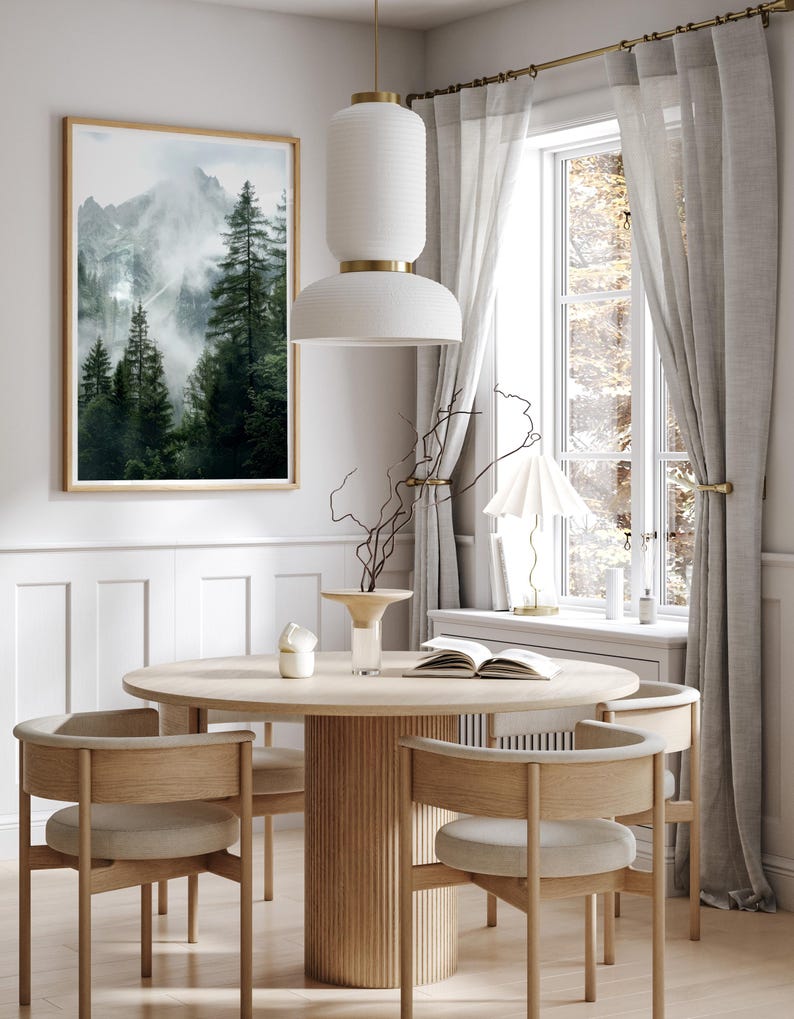 May include: A round wooden dining table with a fluted base and four chairs. The chairs have light brown wood frames and beige upholstery. A framed print of a misty mountain scene hangs on the wall behind the table.