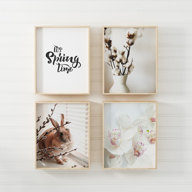 May include: Four framed prints on a white wall. The top left print has the text "It's Spring Time" in black script. The top right print shows a bouquet of white cotton flowers in a white vase. The bottom left print shows a brown rabbit sitting by a window with willow branches. The bottom right print shows white orchids with pink accents.