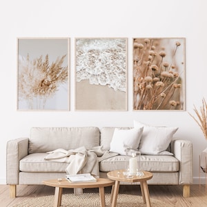 May include: Three framed prints with a neutral colour palette. The prints feature a close-up of dried grasses, a beach scene with white waves crashing on the shore, and a field of dried wildflowers.