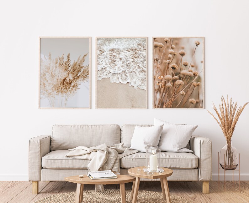 May include: Three framed prints with a neutral colour palette. The prints feature a close-up of dried grasses, a beach scene with white waves crashing on the shore, and a field of dried wildflowers.