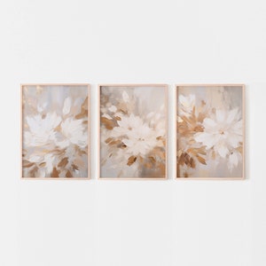 May include: A set of three framed abstract paintings with a floral theme. The paintings feature white and brown brushstrokes on a light gray background.