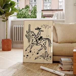 May include: Black and white illustration of a person riding a horse in a desert landscape. The person is wearing a hat and the horse has spots. There are cacti and birds in the background.