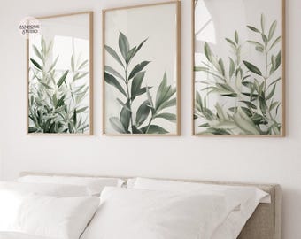 Könnte beinhalten: Drei gerahmte botanische Drucke mit grünen und grauen Blättern in hellbraunen Holzrahmen. Das Kunstwerk wird über einem Bett mit weißer Bettwäsche ausgestellt. Die Drucke stammen von "JAMHOME STUDIO".
