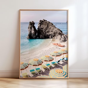 Puede incluir: Una fotograf&iacute;a enmarcada de una escena de playa con sombrillas rayadas de colores y tumbonas. La playa est&aacute; rodeada de acantilados rocosos y agua turquesa.