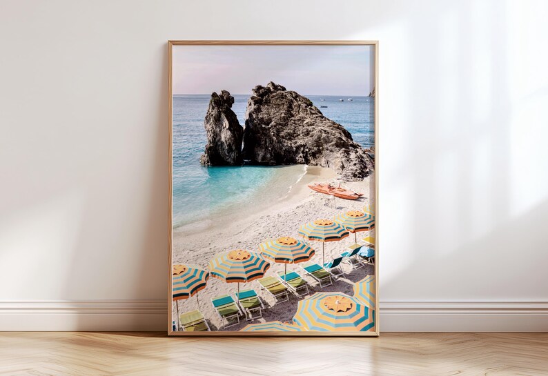 Puede incluir: Una fotograf&iacute;a enmarcada de una escena de playa con sombrillas rayadas de colores y tumbonas. La playa est&aacute; rodeada de acantilados rocosos y agua turquesa.