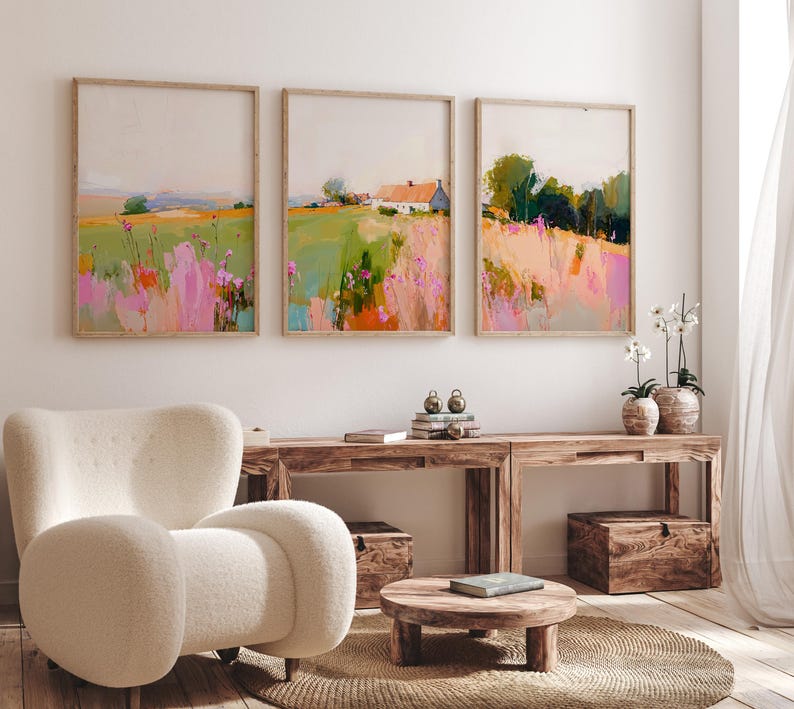 May include: Three framed landscape paintings displayed in a row, featuring abstract fields with pink, green, and orange brushstrokes. The center painting depicts a small white house with a red roof nestled within the colorful meadow scenery.
