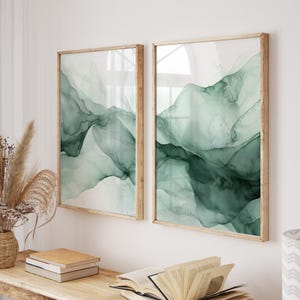 May include: Two framed abstract art prints featuring a green watercolour design. The prints are in wooden frames and are hanging on a white wall.