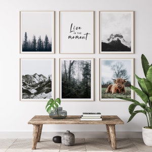 May include: A set of six framed prints featuring nature scenes. The prints include a mountain range, a forest, a cloudy mountain peak, a forest with fog, a highland cow, and a text print that reads "Live in the moment".