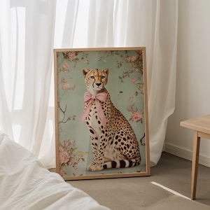 May include: A framed print of a cheetah wearing a pink bow, sitting against a floral background. The cheetah is looking directly at the viewer.