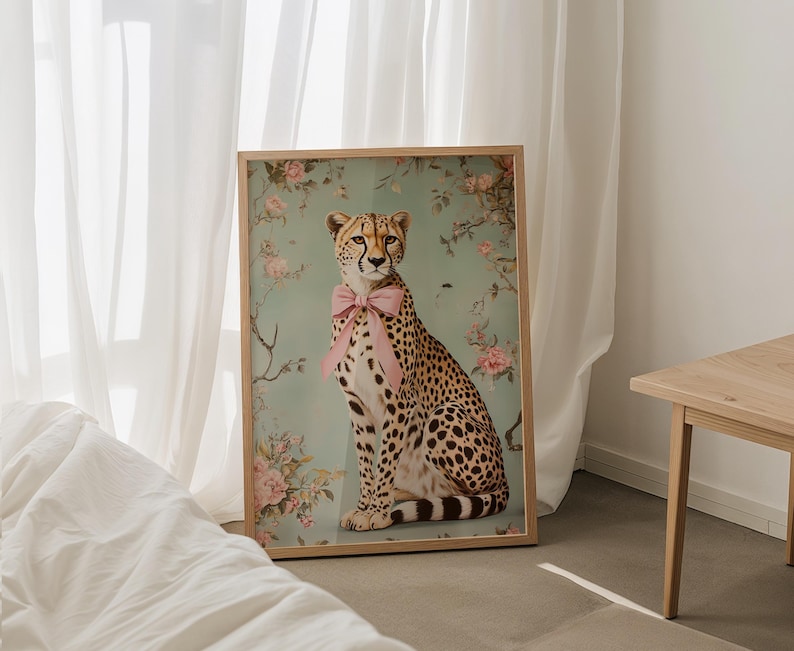 May include: A framed print of a cheetah wearing a pink bow, sitting against a floral background. The cheetah is looking directly at the viewer.