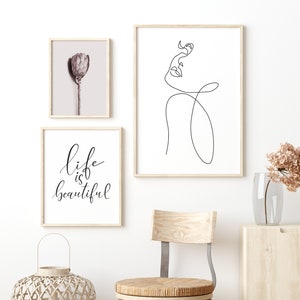 May include: Three framed prints on a white wall. The print on the left features a close-up of a dried flower. The print in the middle features a line drawing of a woman's face. The print on the right features the text "life is beautiful".