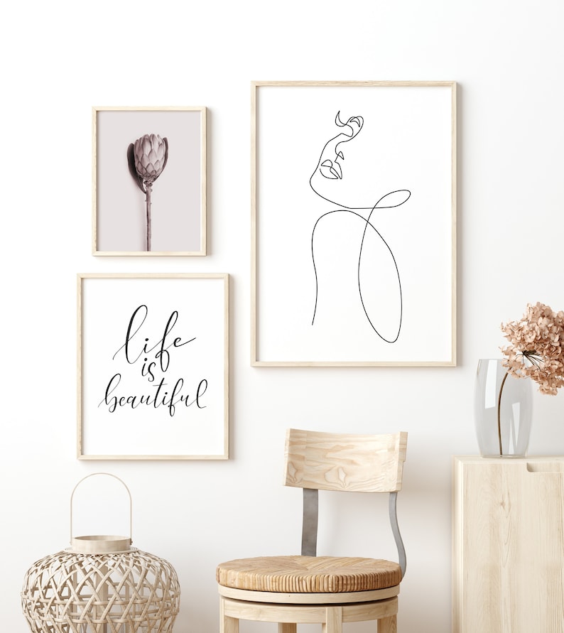 May include: Three framed prints on a white wall. The print on the left features a close-up of a dried flower. The print in the middle features a line drawing of a woman's face. The print on the right features the text "life is beautiful".