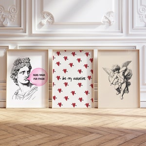 May include: Three framed prints with Valentine's Day themes. The left print features a black and white illustration of a man blowing a bubble that says "More Amor Por Favor". The center print has a white background with a repeating pattern of red hearts with arrows. The text "be my valentine" is in the center of the print. The right print features a black and white illustration of a cherub with wings and an arrow.