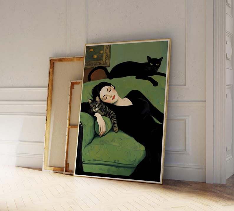 May include: A framed art print depicts a woman in a black dress reclining on a green sofa with a tabby cat. A black cat rests on the sofa's back. The artwork has a vintage aesthetic, with a gold frame and a neutral background.