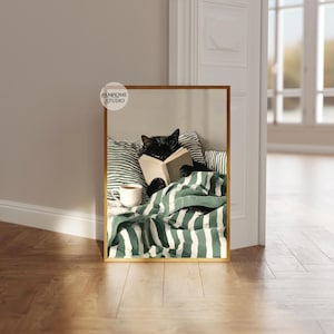 May include: A framed print featuring a black cat reading a book in bed. The cat is nestled under a green and white striped blanket, with a cup of coffee nearby. The print has a gold frame and the text "DAMHOME STUDIO".