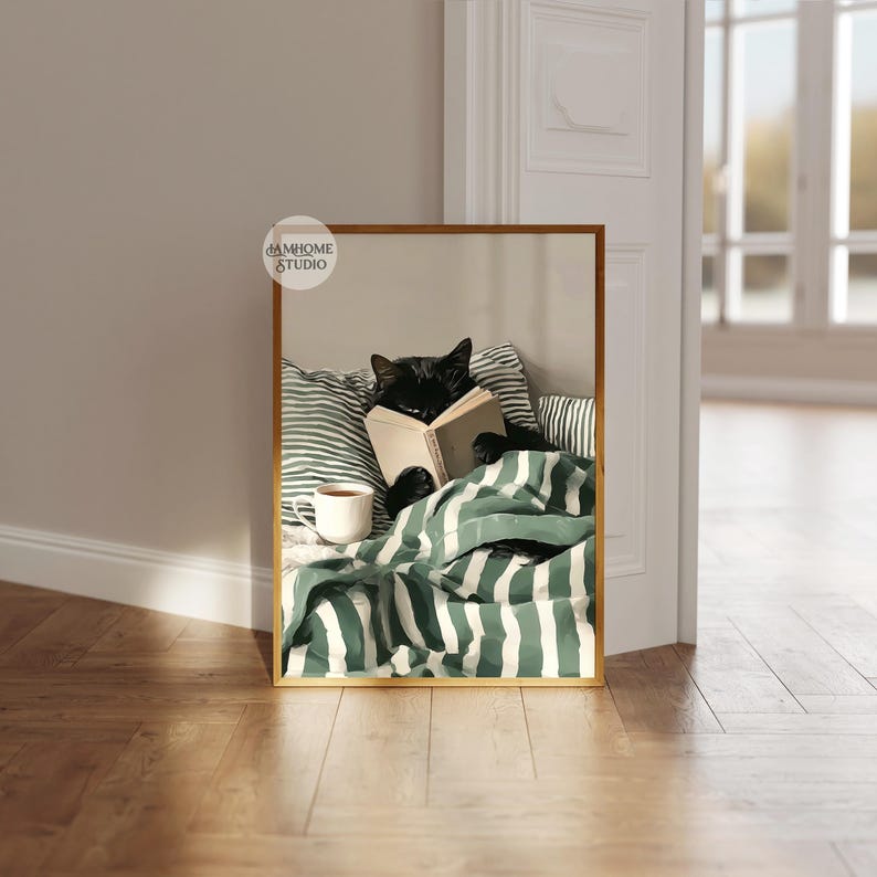 May include: A framed print featuring a black cat reading a book in bed. The cat is nestled under a green and white striped blanket, with a cup of coffee nearby. The print has a gold frame and the text "DAMHOME STUDIO".