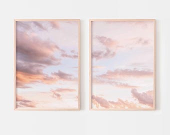 May include: Two vertical rectangular wall art prints in light wood frames, each displaying a photograph of a soft pastel sky at sunset with scattered clouds in shades of pale pink, peach, and light blue against a bright, clear atmosphere.