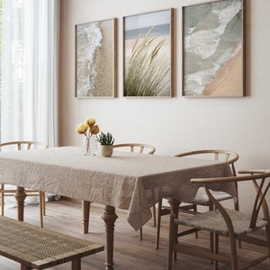 May include: A dining room with a light brown wooden table and chairs, a light brown wooden bench, and a beige tablecloth. Three framed prints of beach scenes hang on the wall behind the table.