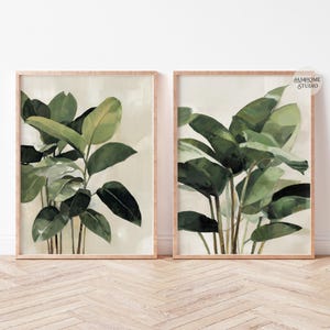 Puede incluir: Dos impresiones bot&aacute;nicas enmarcadas con plantas de hojas verdes. La obra de arte tiene un fondo beige claro y un marco de madera natural. Las impresiones se exhiben sobre un suelo de madera clara contra una pared blanca.
