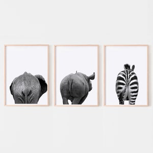 May include: Set of three framed black and white animal prints. The prints feature the rear views of an elephant, a rhinoceros, and a zebra. The frames are a light wood color, and the background is white.