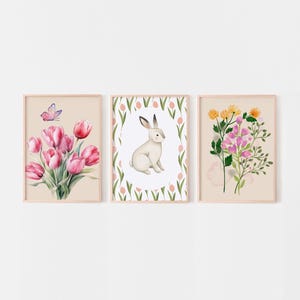 May include: Three framed prints with watercolor illustrations of flowers and a rabbit. The first print features a bouquet of pink tulips with a butterfly. The second print features a white rabbit sitting in a circle of pink tulips. The third print features a bouquet of pink and yellow flowers.