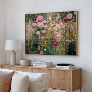 May include: A rectangular wall art print featuring a dense, impressionistic garden scene filled with pink, white, yellow, and red flowers against a deep green foliage background, framed in a light-toned wood border and displayed on a white wall.