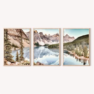May include: Three framed landscape prints featuring mountain and lake scenes. The prints showcase majestic mountains reflected in calm, blue waters, surrounded by lush green forests. The frames are a light wood color.