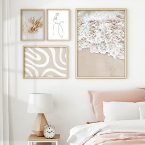 May include: Four framed prints on a white wall above a bed with a white and pink bedding set. The prints feature a wave crashing on a beach, a line drawing of a face, a line drawing of abstract shapes, and a photo of dried pampas grass.