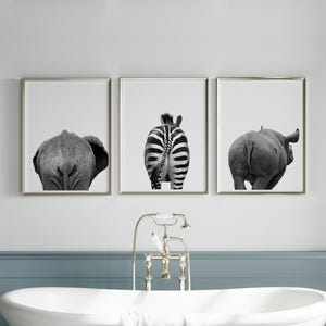 May include: Set of three framed black and white prints featuring the rear views of an elephant, zebra, and rhinoceros. The artwork is displayed above a white bathtub with a vintage-style faucet.