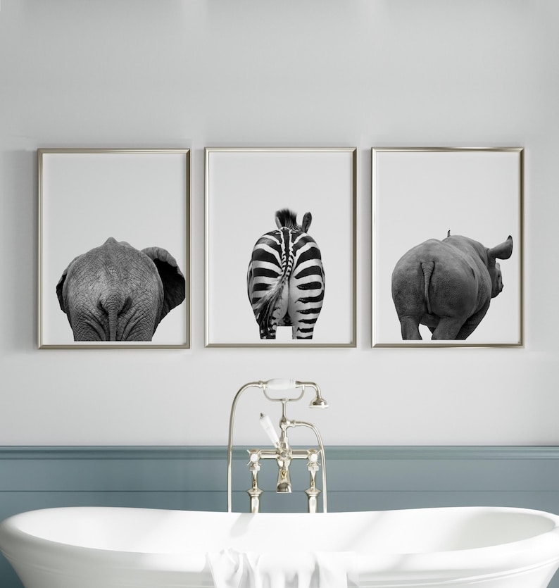 May include: Set of three framed black and white prints featuring the rear views of an elephant, zebra, and rhinoceros. The artwork is displayed above a white bathtub with a vintage-style faucet.