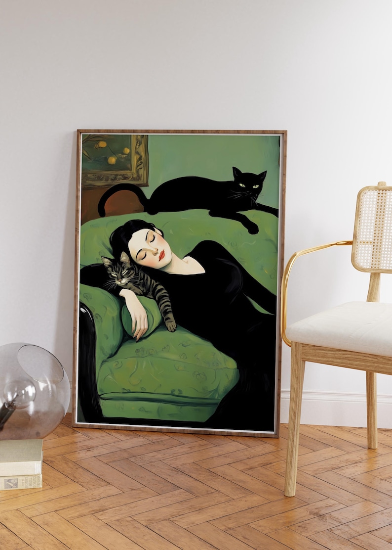 May include: Art print featuring a woman in a black dress reclining on a green sofa with two cats. One cat is resting on the sofa, and the other is lying on the woman. The artwork is framed in a wooden frame.