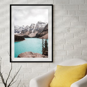 May include: A framed photograph of a mountain lake with snow-capped mountains in the background. The lake is a vibrant turquoise blue and the mountains are a soft brown and white.