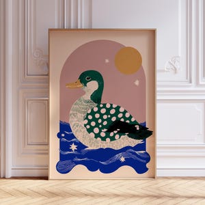 May include: A framed art print depicting a stylized duck. The duck has a green head and back with white polka dots, a yellow beak, and is set against a pink and blue background with a sun and stars.