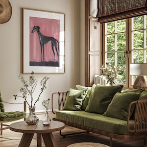 Puede incluir: Interior de sal&oacute;n con una obra de arte enmarcada de un galgo sobre un fondo rosa. La habitaci&oacute;n incluye un sof&aacute; verde con cojines, una mesa de centro de madera y un otom&aacute;n tejido. Una persiana de bamb&uacute; cubre la ventana.