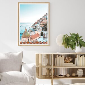 May include: A framed photograph of a colorful Italian village built on a hillside overlooking the ocean. The village is a mix of pastel pink, yellow, and white buildings with terracotta roofs. A large, domed church with a tiled roof is in the foreground.