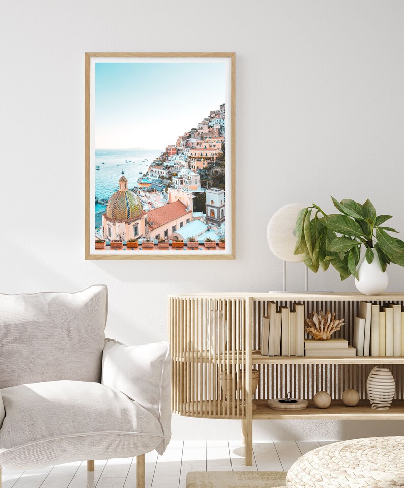 May include: A framed photograph of a colorful Italian village built on a hillside overlooking the ocean. The village is a mix of pastel pink, yellow, and white buildings with terracotta roofs. A large, domed church with a tiled roof is in the foreground.