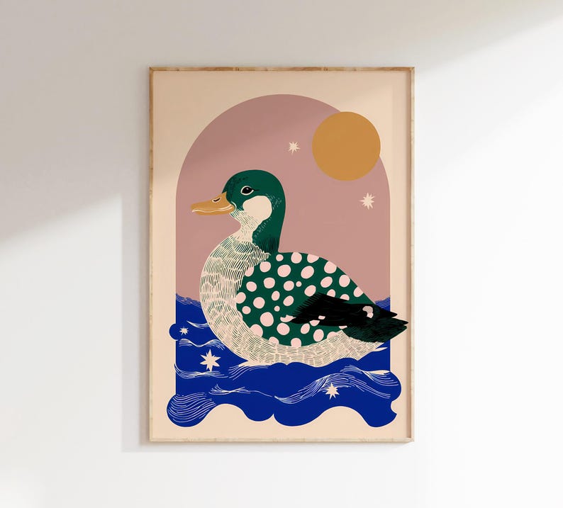 May include: Framed art print depicting a duck with a green head and a body covered in white polka dots. The duck is on blue water, with a pink arch, a yellow sun, and stars. The artwork is in a frame.