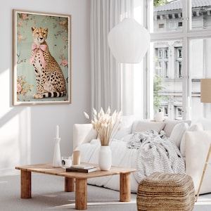 May include: A framed print of a cheetah wearing a pink bow tie, sitting on a light blue background with pink flowers. The cheetah is looking to the right. The print is hanging on a white wall in a living room setting.