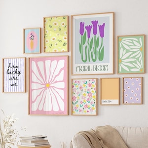 May include: A gallery wall with nine framed prints featuring floral designs. The prints are in various colors, including pink, yellow, green, purple, and white. The prints are arranged in a grid pattern on a white wall.