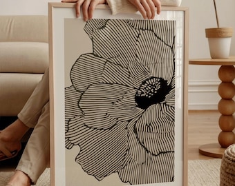 May include: A framed floral art print featuring a large black and white flower design. The artwork has a beige background and is held by a person. The frame is light-colored wood. The print has the text "JAMHOME STUDIO" at the bottom.