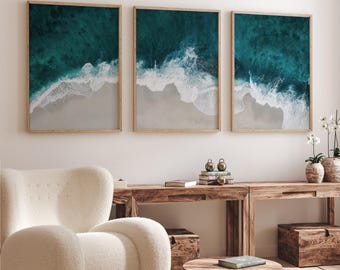 Könnte beinhalten: Ein Set aus drei rechteckigen Wandbildern mit einer Luftaufnahme von türkisfarbenen Meereswellen, die auf einen Sandstrand treffen. Jeder Druck ist in einem hellen Holzrahmen gefasst und zeigt tiefblaues Wasser und weißen Schaum.