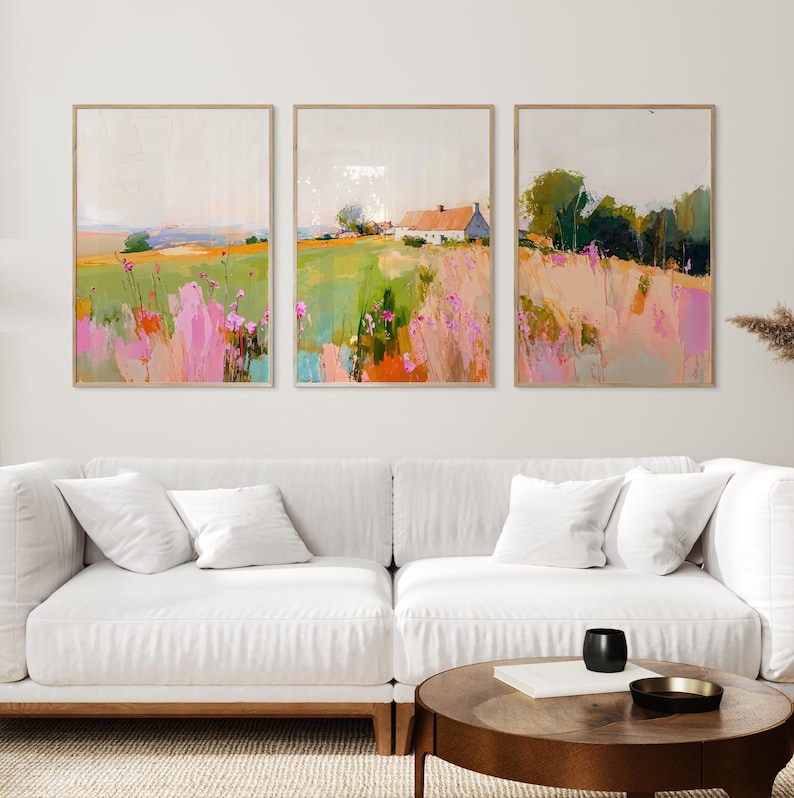 May include: A set of three rectangular wall art prints featuring impressionistic landscape paintings. The artwork displays fields of green grass, pink wildflowers, and a white house with a roof, rendered in soft, blended brushstrokes and colors.