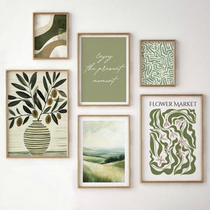May include: A collection of six framed art prints with gold frames. The prints feature various designs, including abstract shapes, botanical illustrations, and landscape paintings. One print has the text "Enjoy the present moment" in cursive. Another print says "Flower Market".
