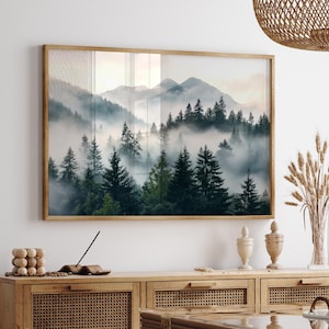 May include: A framed landscape print featuring a misty forest scene with mountains in the background. The artwork showcases a serene view of evergreen trees shrouded in fog, with a wooden frame. The color palette includes shades of green, gray, and brown.