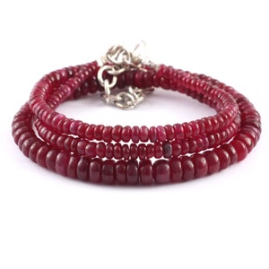 May include: A triple strand necklace made of small, round, red ruby beads with a silver clasp.